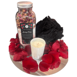 Rose petals with a bath soak jar, candle, and black bath pouf on a tray
