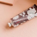 Tube of Lollia hand cream on a peach fabric surface