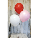 Three helium balloons in red, pink, and white against a streamered backdrop.