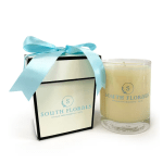 Cream-colored candle in a glass jar beside a white gift box with a blue ribbon