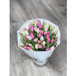 Bouquet of pink and white tulips wrapped in white paper and displayed in a clear glass vase