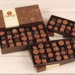 Three boxes of assorted chocolates on a light wood surface
