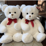 Two white teddy bears with red bows sitting side by side