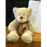 Cream teddy bear with a brown ribbon sitting on a wooden surface