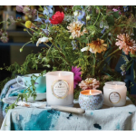 Wildflower arrangement with three lit candles and a turquoise cup on a painted cloth