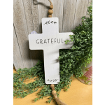 White cross-shaped hanging sign with the word "GRATEFUL" and greenery