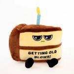 Plush cake-shaped toy with a candle and text reading "GETTING OLD BLOWS!"