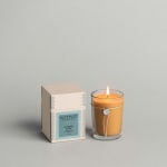 Lit amber candle in a glass tumbler beside its box