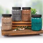 Four scented candles in glass jars on a wooden tray
