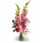 Mixed pink flower arrangement in a clear vase hugged by a white teddy bear.