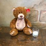 Brown teddy bear with a plaid bow beside a small glass candle