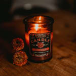 Lit amber candle in a glass jar beside two dried flower heads