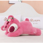 Pink teddy bear plush lying on a bed with decorative pillows