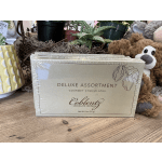 Box of gourmet chocolates beside a plush teddy bear and potted plants