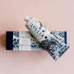 Two Lollia hand cream tubes and a matching box on a pink background