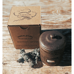 A boxed bourbon vanilla candle beside a rustic metal candle jar on a wooden surface.