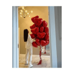 Cluster of red heart-shaped balloons in a room with a woman standing beside them.