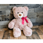 Light pink teddy bear plush with a red bow sitting on a rustic wooden surface.