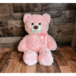 Large pink teddy bear with satin bow sitting against rustic wood background