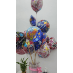 Cluster of birthday balloons in a clear vase with a small potted plant beside it