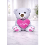 Gray teddy bear holding a pink heart with the word LOVE