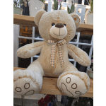 Large beige teddy bear with a plaid bow sitting on a wooden shelf
