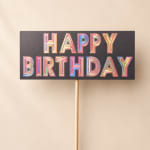 Colorful "Happy Birthday" sign on a stick against a plain background