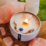 Lit white candle in a round container surrounded by pink stones