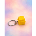 Cheese-shaped yellow keychain on a pastel background