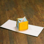Pop-up greeting card with a small yellow and blue paper box centerpiece