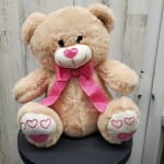 Plush teddy bear with a pink ribbon and heart details