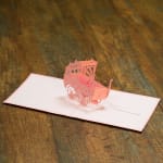 Pink pop-up baby carriage card on a wooden surface