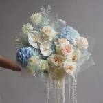 Bouquet of blue hydrangeas, cream roses, and white anthuriums with trailing white accents