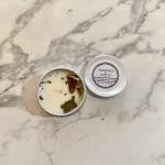 Two small tin candles on a marble surface, one open and one with a label.