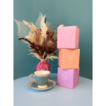 Dried floral arrangement in a pink vase beside stacked tea boxes and a teacup set