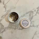 Two small tin candles on a marble surface, one open and one lidded.