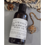 Bottle of geranium body oil with a gold pendant necklace beside it