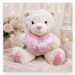 Plush white teddy bear holding a pink heart, with roses in the background.