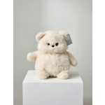 Cream plush teddy bear sitting on a white pedestal