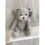 Gray teddy bear with a pink ribbon sitting on fabric