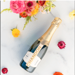 Champagne bottle surrounded by colorful flowers on a light surface