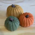 Three knitted pumpkin decorations in green, orange, and tan
