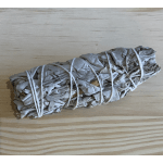 A bundled sage smudge stick tied with white string on a wooden surface