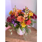 Mixed bouquet of pink, orange, yellow, and purple flowers in a white vase
