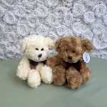 Two plush teddy bears sit in front of a white rose wall.