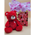 Red teddy bear beside a heart-patterned gift bag with tissue paper