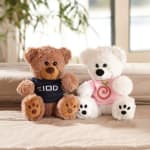 Two teddy bears in shirts sitting on a bed