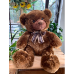 Brown teddy bear with a plaid bow sitting on a wooden table