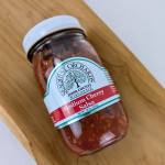 Jar of medium cherry salsa with a white lid on a wooden board
