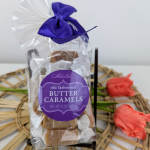 Bag of butter caramels tied with a purple ribbon beside coral tulips